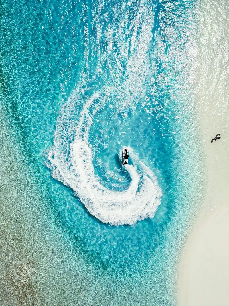 A jet ski drawing a foamy trail on turquoise water, aerial view