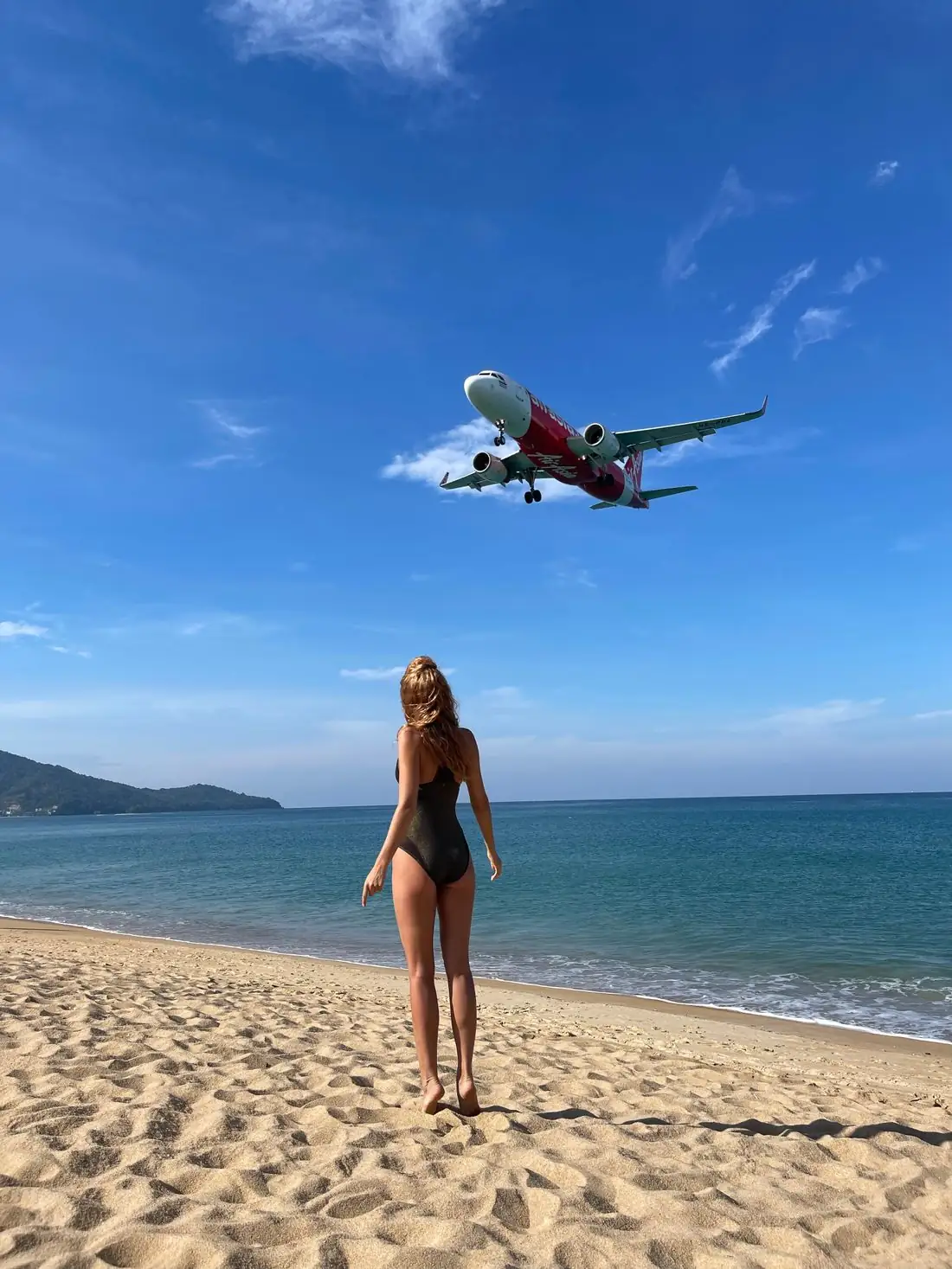 A woman on Mai Khao Beach as a plane comes in to land overhead